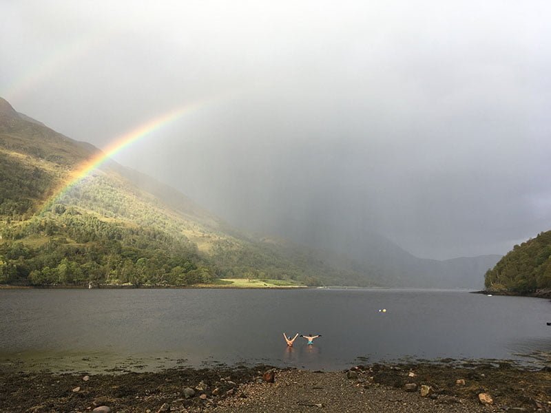 Swimmers in a grey sea below a rainbow